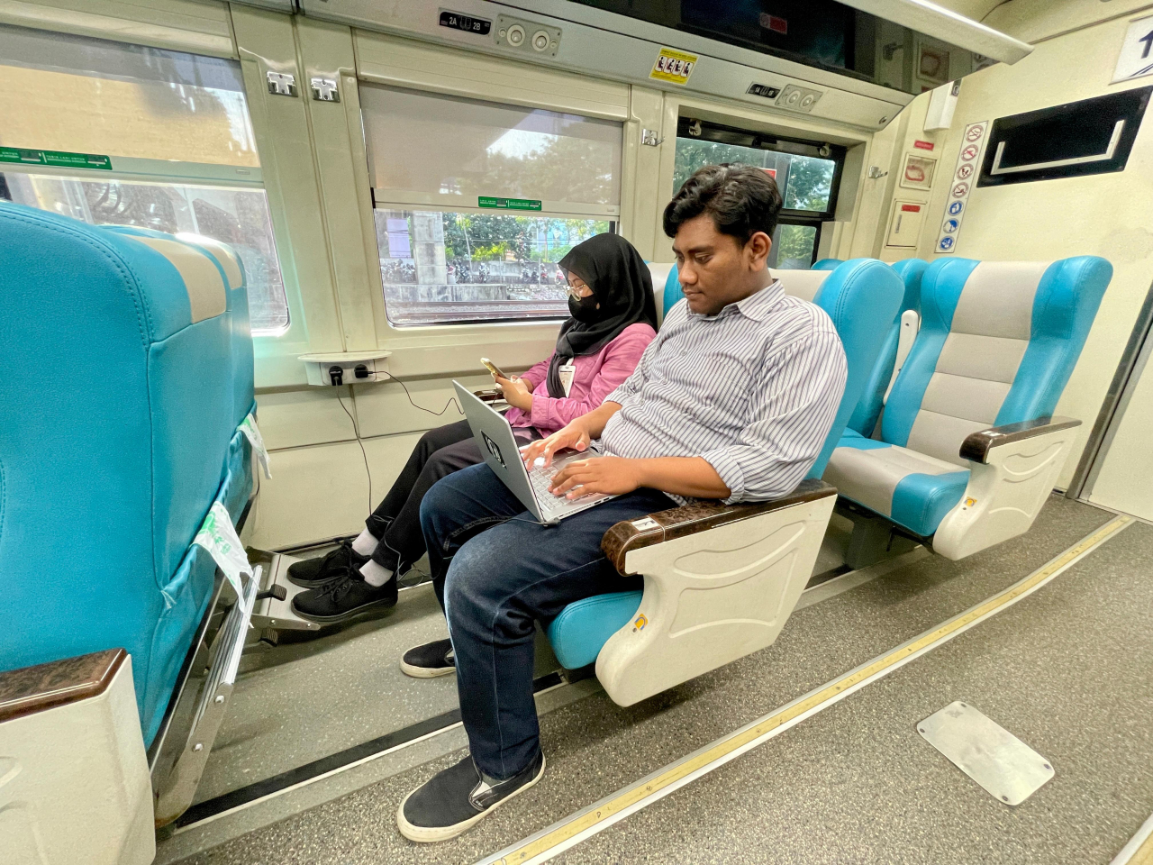 Penumpang menggunakan stop kontak di dalam kereta untuk mengisi baterai laptop. Foto : KAI for Jatimkini