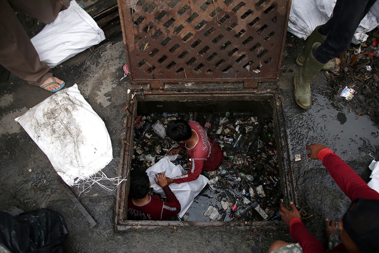 Petugas dari DSDABM Surabaya melakukan pembersihan saluran air yang tersumbat sampah.