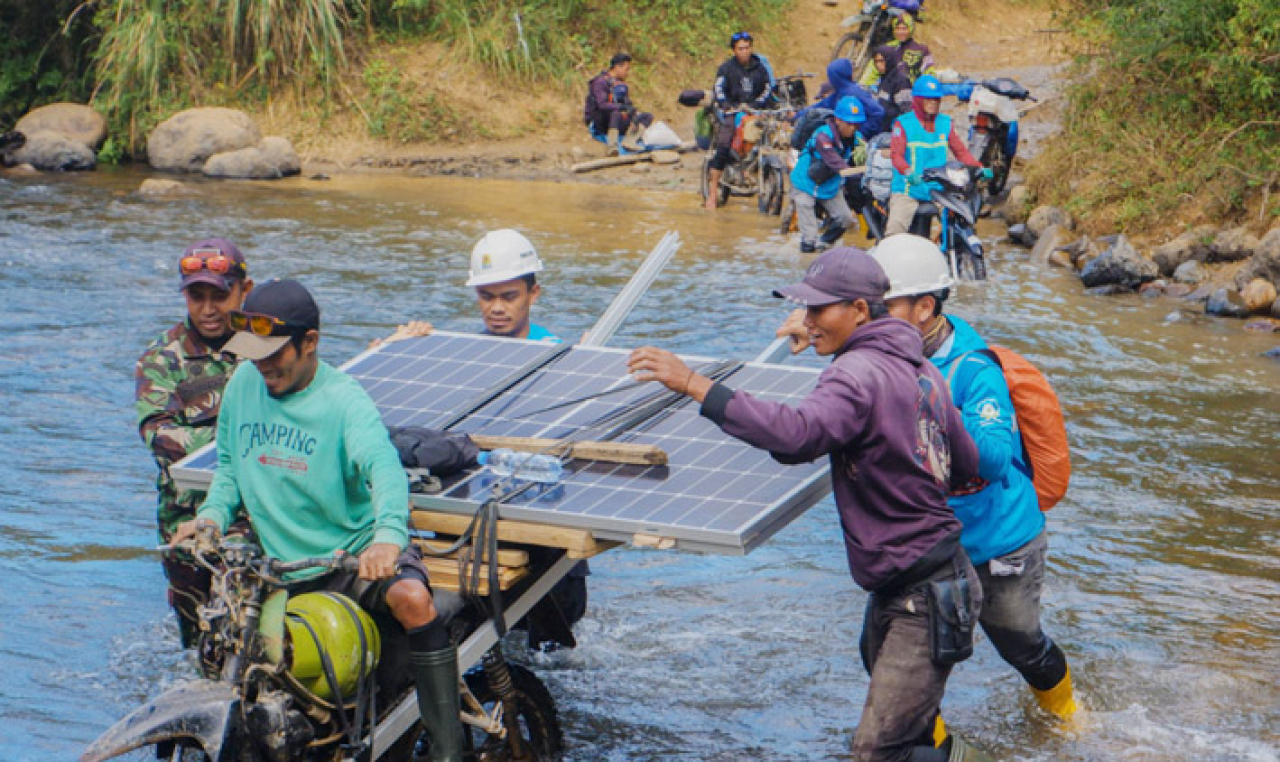 Petugas PLN bersama warga bahu-membahu membawa panel surya melintasi sungai.